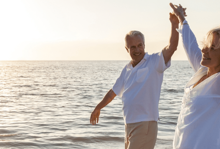 voyager après 50 ans couple levant les bras marchant dans l'eau sur une plage au coucher du soleil