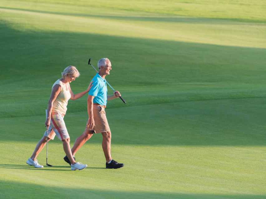 couple après 50 ans en tenue de golf avec leurs clubs marchant sur un green de golf